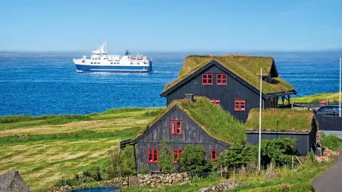 Traditionelle Häuser mit Grassoden-Dächern und Fährschiff auf den Färöer-Inseln mit trendtours Reisen-placeholder